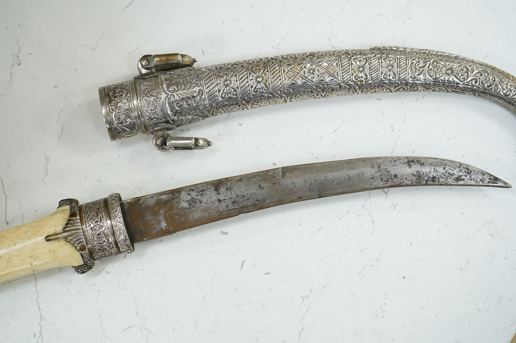 A silver mounted Moroccan dagger jambya, with silver sheath and hilt, mounts chased with foliate and floral designs, and one piece bone grip, blade as found, overall length 42cm
